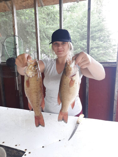 female guest holding up two smallmouth bass
