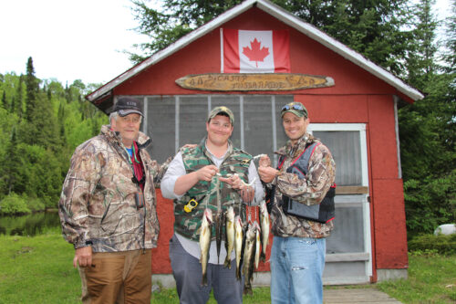 three men with stringer of fish in front of cabin